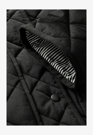 Schwarze gesteppte Jacke mit einem schwarzen Knopf, Fischgrätbesatz und einem gestreiften schwarz-weißen Innenfutter. Strukturiertete Außenseite.