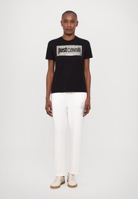 Svart bomull t-skjorte med et sølvfarget logo i zebra-striper. Kombinert med hvite bukser med en naglet bokstavdesign og beige sneakers.