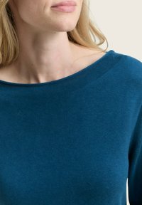 Azurblauwe trui van zacht gebreide stof, met een brede halslijn en een gladde textuur, met de nadruk op comfort en een casual pasvorm.