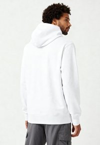 Felpa bianca con una texture morbida, caratterizzata da un grande cappuccio, polsini a coste e un taglio rilassato, abbinata a pantaloni cargo grigi.