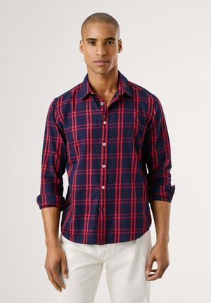 Camisa de cuadros en azul marino para hombre con patrones en rojo y blanco, con botones frontales y mangas enrolladas. Fabricada en tela ligera.