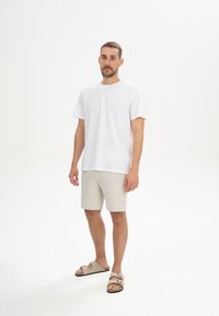Witte katoenen t-shirt, beige shorts en beige sandalen. Eenvoudig ontwerp, ontspannen pasvorm, korte mouwen en platte zool schoenen.