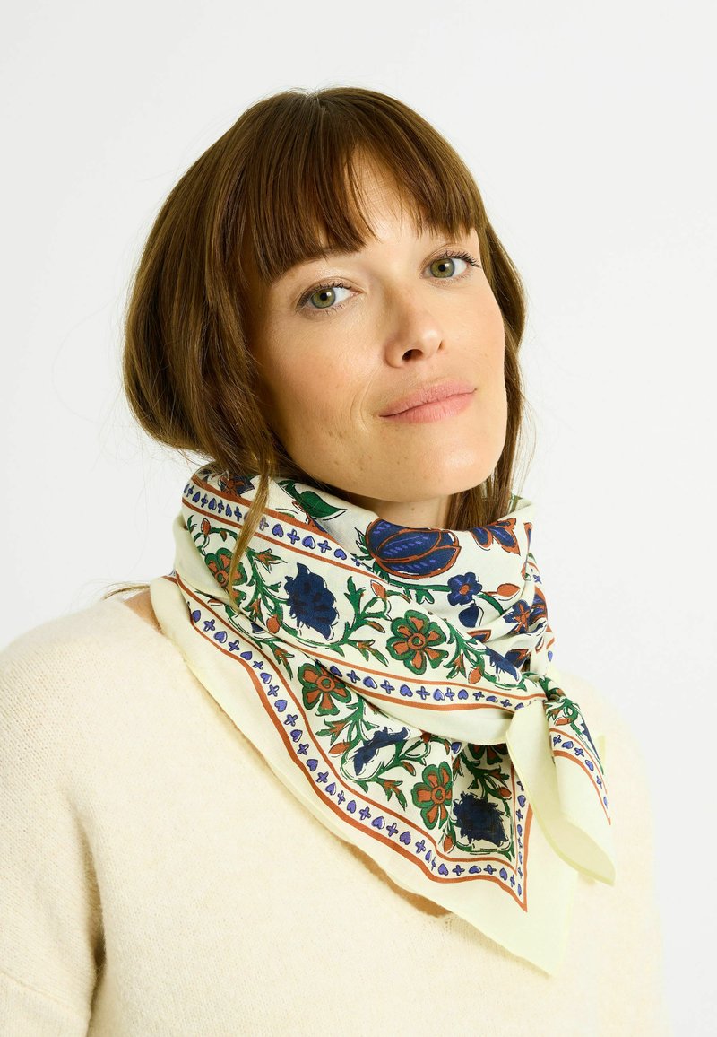 Pañuelo de seda con patrones florales en azul, rojo y verde sobre un fondo crema; presenta un detalle anudado en la parte frontal.