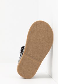 Czarna sandały z teksturowaną gumową podeszwą, z gładkim materiałem wierzchnim i regulowanym paskiem. Podeszwa ma jasnobrązowy kolor.