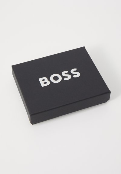 Boîte rectangulaire noire avec une texture lisse et un logo "BOSS" blanc sur le dessus. Design minimaliste, sans motifs ni accents supplémentaires.