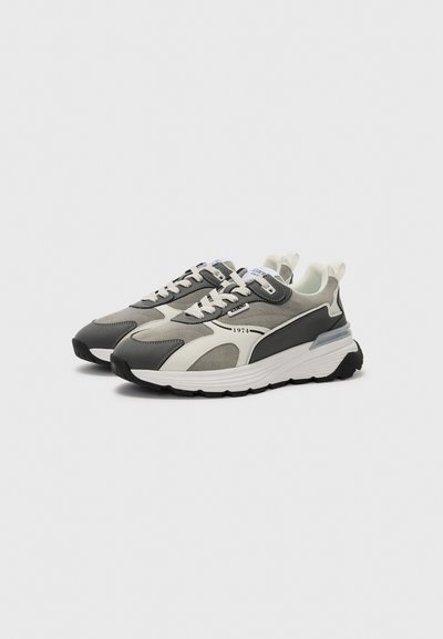 Scarpe da sport in grigio e bianco, con una tomaia testurizzata, suola imbottita e dettagli a contrasto, design con lacci e maniglia per il trasporto.