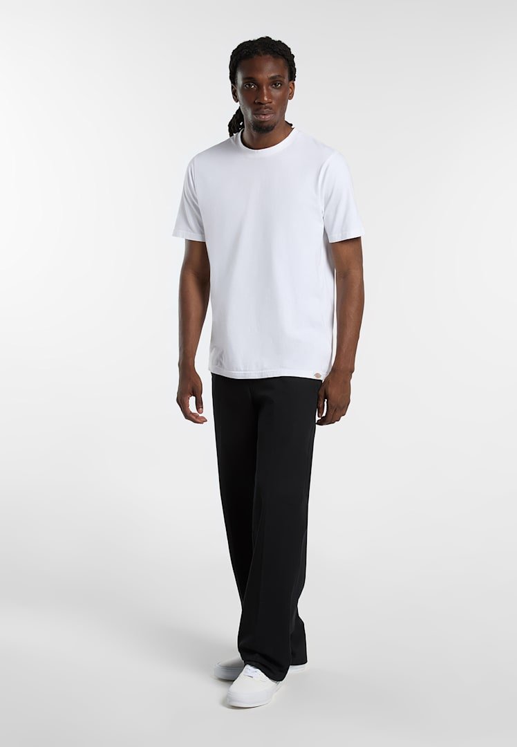 Uomo in piedi che indossa una maglietta bianca semplice, pantaloni neri e scarpe da ginnastica bianche su uno sfondo bianco.
