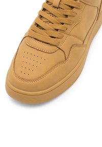 Brązowy sneaker z perforowanym noskiem, teksturowanymi sznurowadłami i szczegółowym przeszyciem na białym tle.