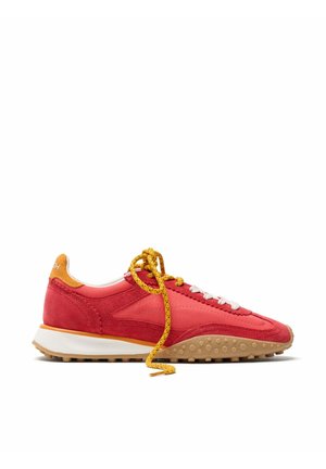 Zapatilla baja roja y naranja con cordones amarillos y suela de goma, vista de lado sobre un fondo blanco.