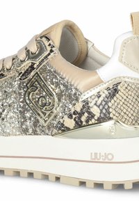 Baskets Liu Jo avec une tige en paillettes beiges et dorées, des accents en simili cuir serpent, des détails en or, et une semelle blanche avec une semelle extérieure antidérapante.