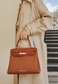 Sac à main marron au design structuré, doté d'une poignée supérieure en cuir, de quincaillerie dorée et d'un corps en tissu texturé.