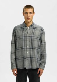 Hallide hallide särk tumesiniste aktsentidega, nööpidega kinni pandud disain, pikad varrukad, pehme tekstuur ja standardne krae; kantud tumedate teksadega.