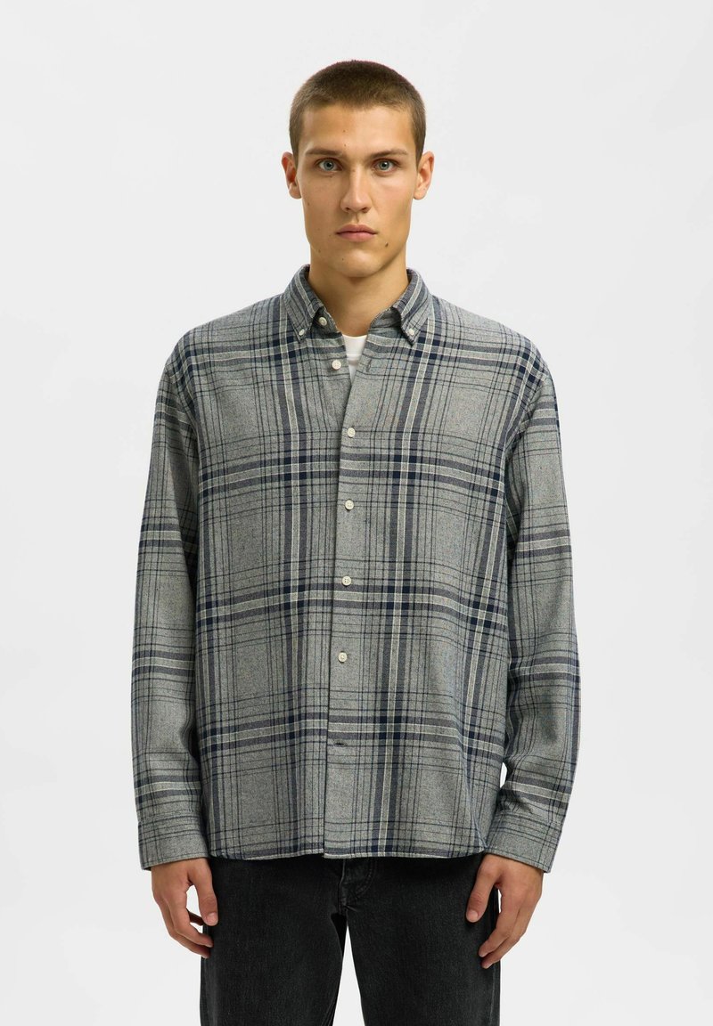 Hallide hallide särk tumesiniste aktsentidega, nööpidega kinni pandud disain, pikad varrukad, pehme tekstuur ja standardne krae; kantud tumedate teksadega.