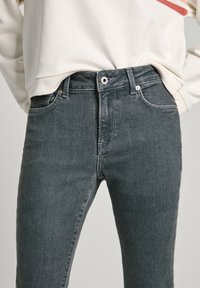 Šedé džíny z denimu s úzkým střihem, pěticípým designem a viditelným prošíváním. V kombinaci se světlým krémovým svetr.