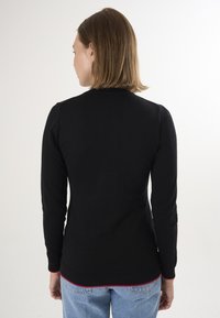 Schwarzer Strickpullover mit langen Ärmeln, gerippten Bündchen und rotem Akzent am Saum, ausgestattet mit einer figurbetonten Passform und glatter Textur.