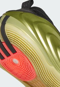 Semelle d'une basket sportive avec une accroche rouge texturée, une semelle intermédiaire jaune et vert olive, et une tige en tissu noir avec languette de talon.