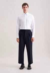 Wit overhemd met knopen en een klassieke kraag, gecombineerd met brede, marineblauwe geplooide broek. Zwarte schoenen maken de outfit compleet. Soepele stoftextuur.