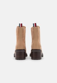 Botines de ante beige con un acabado texturizado, tacón cuadrado marrón y una tira de tracción a rayas en rojo, blanco y azul en la parte trasera.