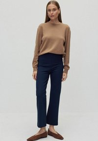 Beige gebreide trui, hoogtaille donkere blauwe broek en bruine suède ballerina's. Eenvoudig ontwerp met een ontspannen pasvorm en lange mouwen.