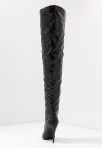 Botas negras de charol hasta la rodilla con un patrón de cocodrilo texturizado, punta afilada y un alto tacón de aguja.