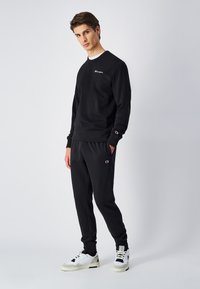 Sæt bestående af sort sweatshirt og bukser lavet af blødt stof, med ribbede manchetter, rund halsudskæring og et lille logo på brystet og bukserne.