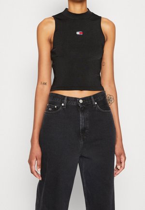 Sort ærmeløs crop top med høj krave og lille rød, hvid og blå "Tommy Jeans" logo på brystet; båret med høj talje sorte jeans.