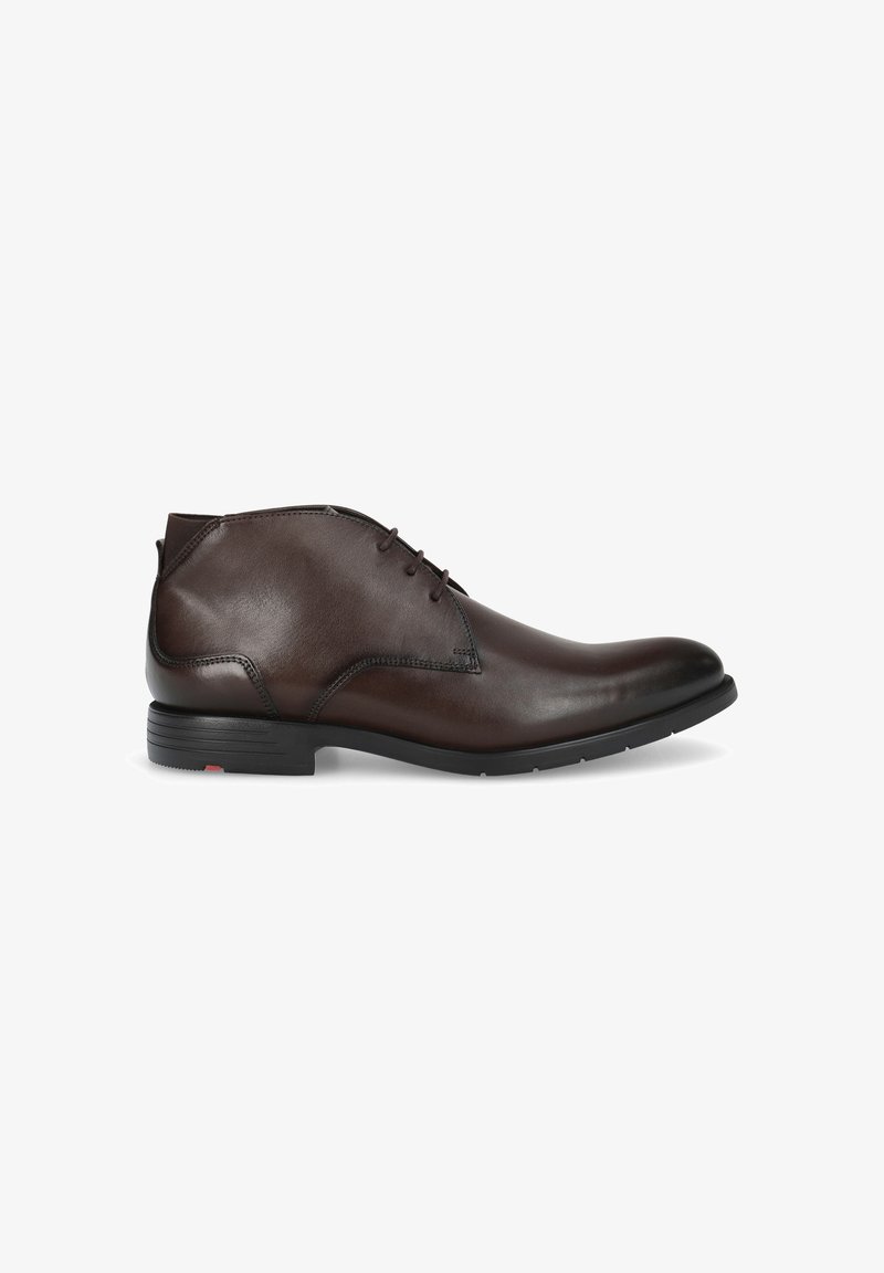 Bottines en cuir marron avec une texture lisse, bout rond et trois œillets pour les lacets. Présente une semelle en caoutchouc noire contrastante.