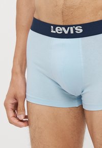 Ljusblå bomullsboxershorts med midja i marinblått som har en vit "Levi's"-logotyp, slät textur och figurnära design.