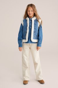 Zināmu džinsu bezrūpīgu jaku ar baltu mākslīgo kažokādu un divām priekšējām kabatām, valkā pār zilu krekli. Apvienots ar beige biksēm un brūnām kurpēm.