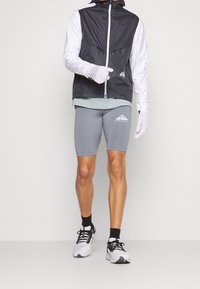 Veste légère noir et blanc avec capuche, tee-shirt gris à manches courtes, shorts gris ajustés et chaussures de sport blanches avec des accents noirs.