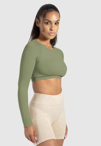 Olijfgroene cropped langemouwen top met een ronde halslijn, gecombineerd met hoge beige shorts. Gladde textuur, aansluitend ontwerp.