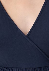 Námořnická modrá šaty s hlubokým V výstřihem a zavinovacím designem, vyrobené z měkké, strukturované tkaniny, s nařasením v oblasti pasu.