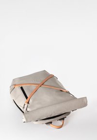 Grijze roll-top rugzak met leren riemen. Heeft een slank ontwerp, een soepele textuur en een externe ritszak. Handgrepen aan de bovenkant.