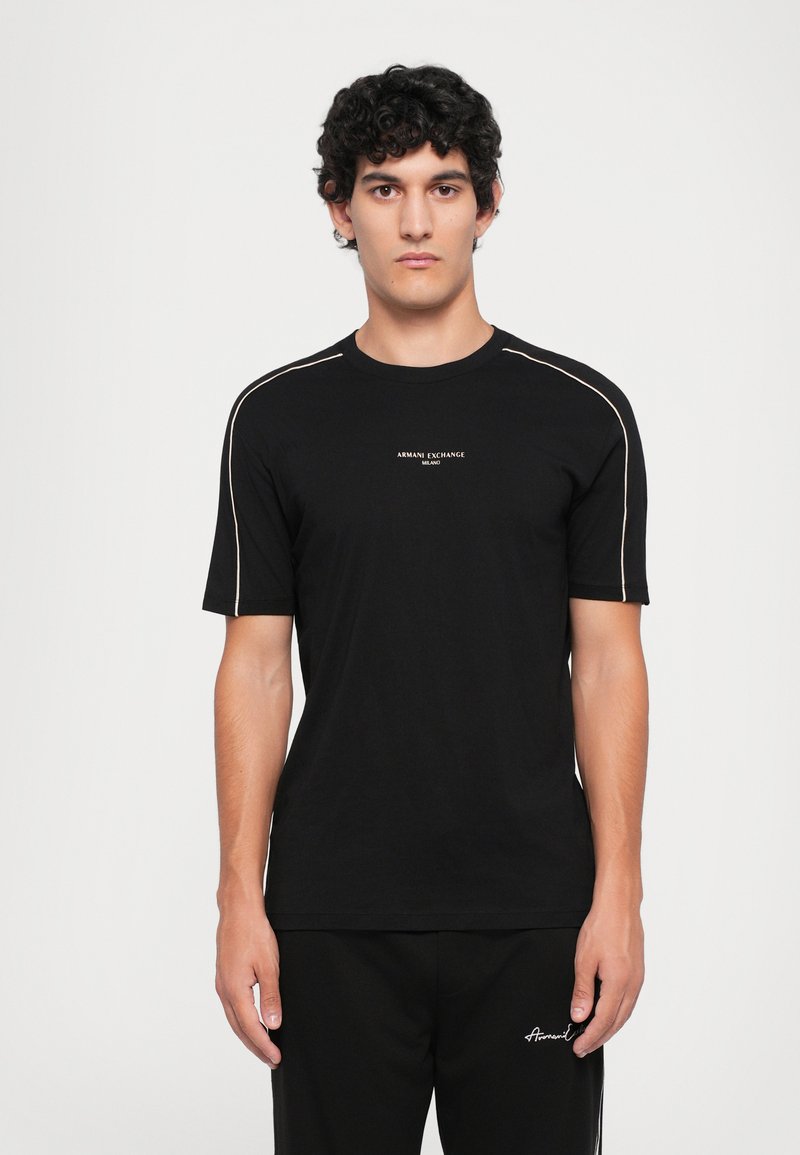 Svart T-skjorte med korte ermer laget av bomull, med hvite sømdetaljer. Den har en liten logo på brystet og er designet med slim fit.