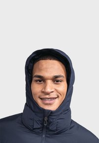 Dunkelblaue Kapuzenjacke mit hohem Kragen, ausgestattet mit einem Reißverschluss vorne und weichem, strukturiertem Stoff. Das charakteristische Kapuzendesign bietet umfassenden Schutz.