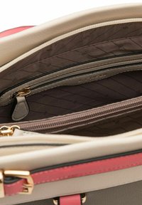 Intérieur de sac à main en cuir beige et rose avec une doublure en tissu foncé à motif losange, deux poches zippées et des accents en métal doré.