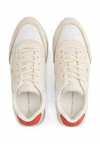 Sneakers beige con tomaia in pelle textured e accenti bianchi. Presentano una toppa rossa sul tallone e lacci tonali. Dettaglio del logo discreto sulla soletta.