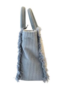 Vertical blauwe handtas met ribbelstof textuur, franjes aan de zijkanten en korte, gewatteerde handvatten. Geschikt voor casual gebruik.