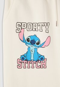 Biała tkanina z niebieską postacią z kreskówki o dużych uszach i oczach, siedzącą pod napisem "SPORTY" i "STITCH" w czarnym i różowym kolorze.