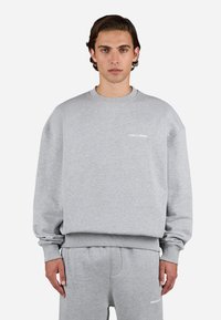 Grå sweatshirt lavet af bomuldsblanding med rund halsudskæring og ribbede manchetter. Har et lille hvidt logo på brystet og en afslappet pasform.
