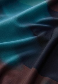Weicher Stoff mit Falten in den Farbtönen teal, dunkelblau und braun, der eine glatte Textur und sanfte Beleuchtung zeigt.