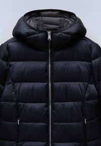 Sort puffer-jakke med hætte, med et quiltet design, lynlås lukning og to sidelommer med lynlås. Glat, skinnende stofstruktur.