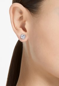 Runde studøredobber med en stor sentral klar stein, omgitt av mindre glitrende steiner i en sølvfarget innfatning.