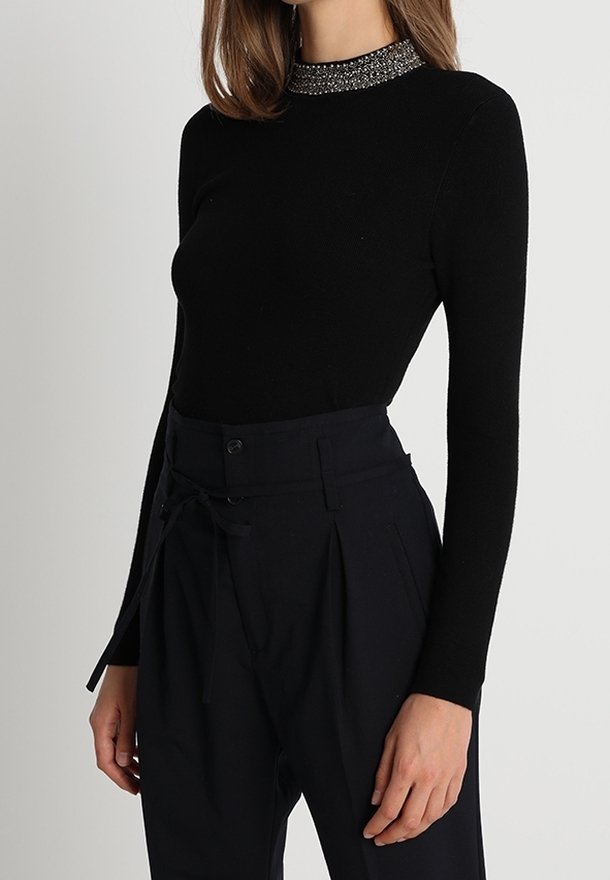 Maglia nera a maniche lunghe con scollatura decorata, abbinata a pantaloni scuri in navy a vita alta con chiusura a fiocco e tasche laterali.