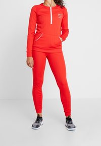 Ensemble sportif rouge composé d'un haut à demi-fermeture éclair avec poche kangourou et de leggings ajustés assortis. Comprend des accents blancs et une texture côtelée.