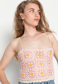 Top cropped de crochet com uma base em creme e padrões florais quadrados em rosa e amarelo, alças ajustáveis e bordas em forma de onda.