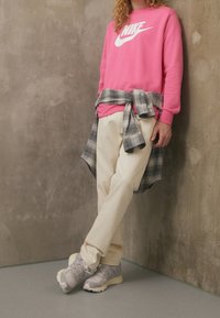 Ljust rosa Nike sweatshirt, krämfärgade byxor, grå sneakers med textur, och en lös grå rutig skjorta knuten runt midjan.