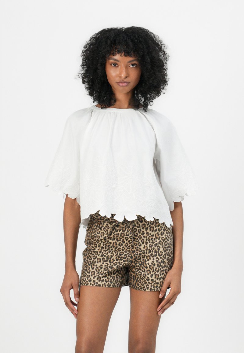Blouse blanche brodée avec des manches évasées et un ourlet festonné, accompagnée de shorts à imprimé léopard avec une taille à cordon.