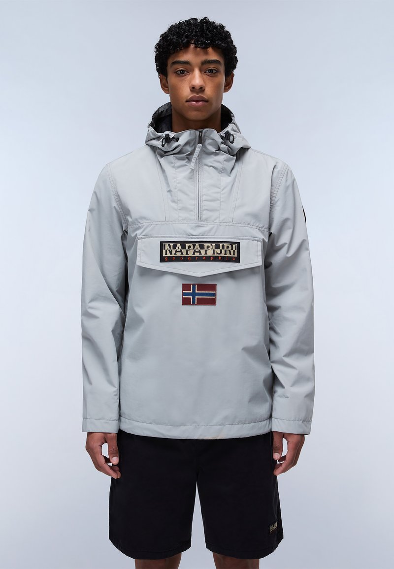 Ljusgrå fuskjacka med en framficka, utrustad med en logotyp och detalj med en norsk flagga. Tillverkad av ett glatt, vattentätt material.