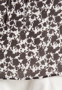 Motif floral noir sur tissu blanc texturé avec un cordon coulissant en haut et tissu blanc partiellement visible en dessous.